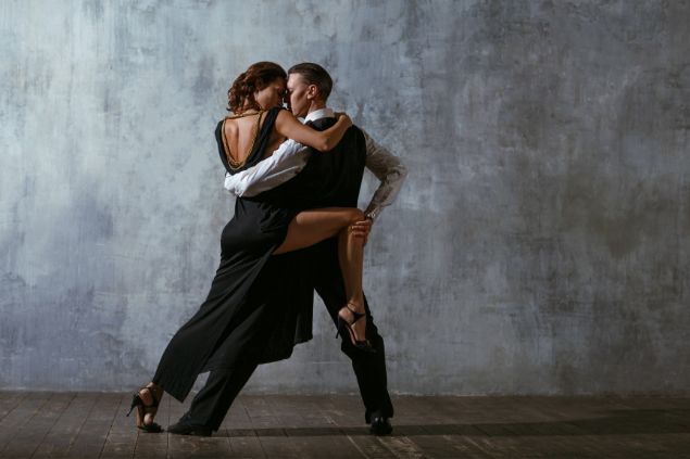 Imagem de um casal dançando tango. Ambos usam roupas pretas e a moça um vestido sensual.