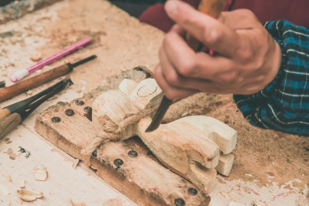 4045 / Getty Images / Canva Imagem de uma pessoa fazendo uma escultura artesanal em madeira.