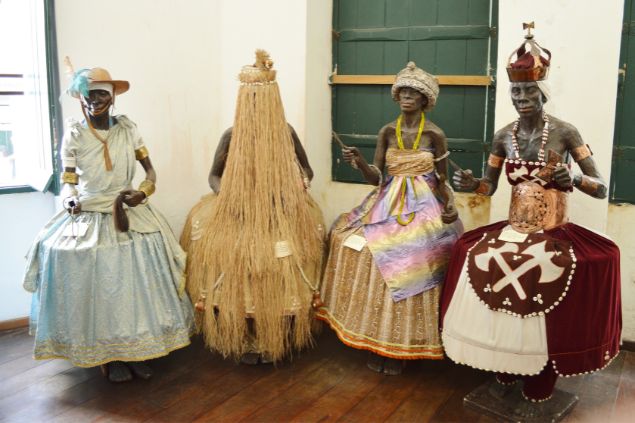 Gustavoboulhosa / Pixabay / Canva Imagem de vários tipos de orixás feitos de cera, expostos em uma sala.