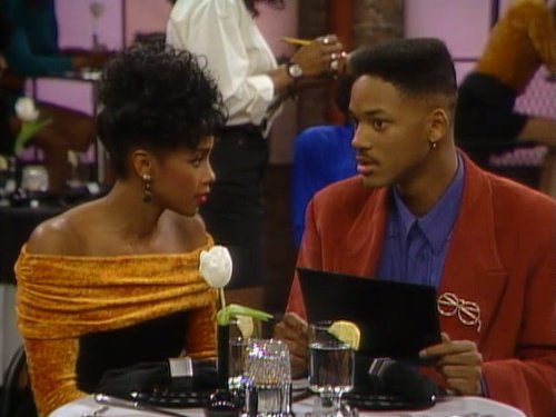 Homem e mulher negros usando roupas coloridas em um restaurante.