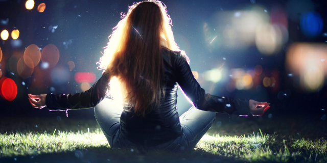 Mulher sentada na grama em meio a sinais iluminados.