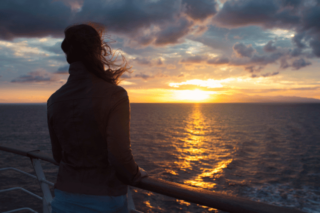 Mulher em navio olhando o pôr do sol no horizonte