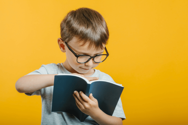 Criança de óculos lendo um livro, em fundo amarelo.
