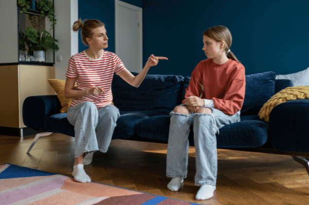 dimaberlinphotos / Canva Pro Mãe e filha sentadas no sofá. A mãe está dando uma bronca enquanto aponta o dedo.