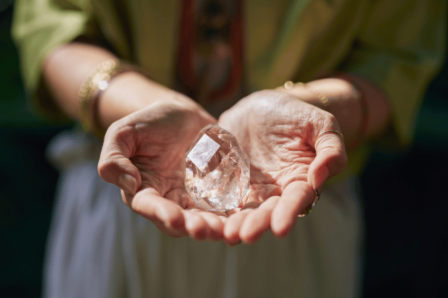 francescoridolfi.com / Rido / Canva Uma mulher está com as mãos juntas segurando um cristal transparente.