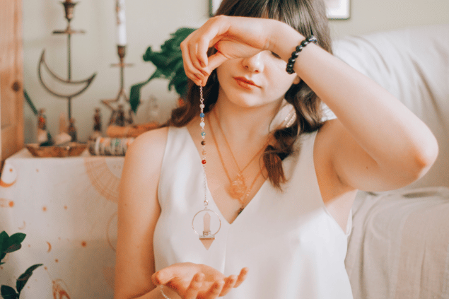 Alina Vilchenko / Pexels / Canva Uma mulher está segurando um cordão com um pingente de cristal na ponta.