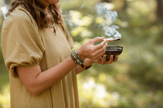 Syda Productions / Canva Uma mulher está queimando palo santo em um ambiente de natureza.