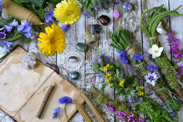 Na imagem, há flores, pedras e um caderno em cima de uma mesa.
