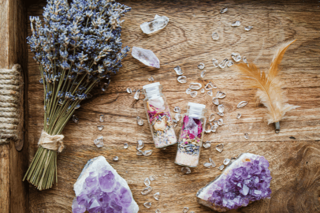 FotoHelin / FotoHelin Images / Canva Na imagem, há dois recipientes com plantas em cima de uma mesa. Além disso, há cristais, penas e flores também.