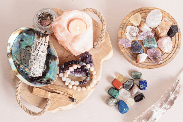 Oksana Vejus / Canva Na imagem, há alguns recipientes com palo santo e pedras em cima de uma mesa. E há uma vela acesa.