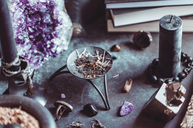 Edalin / Getty Images Pro / Canva Na imagem, há um recipiente com plantas queimadas em cima de uma mesa. E há uma vela e pedras também.