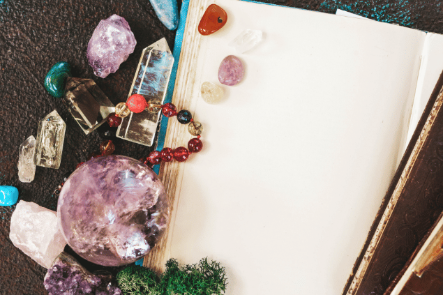 Neirfy / Canva Na imagem, há cristais, plantas e um caderno em cima de uma mesa.