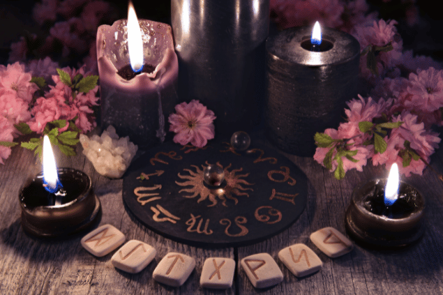 Na imagem, há velas, flores e pedras em cima de uma mesa.