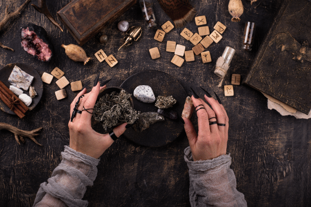 Yuliya Furman / Yuliya Furman / Canva Na imagem, há um recipiente com plantas em cima de uma mesa. Além disso, há pedras, palo santo, pedras de runas e um livro.