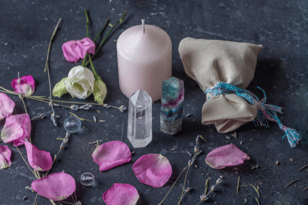 Na imagem, há flores, cristais e uma vela em cima de uma mesa.
