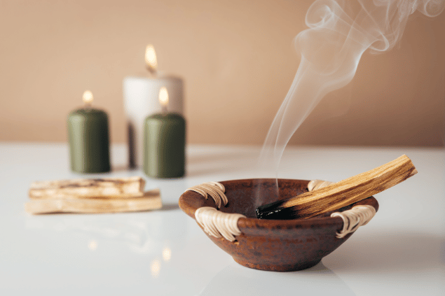 Jasmina Putnik / JRP Studio / Canva Na imagem, há um recipiente com palo santo e velas acesas em cima de uma mesa.