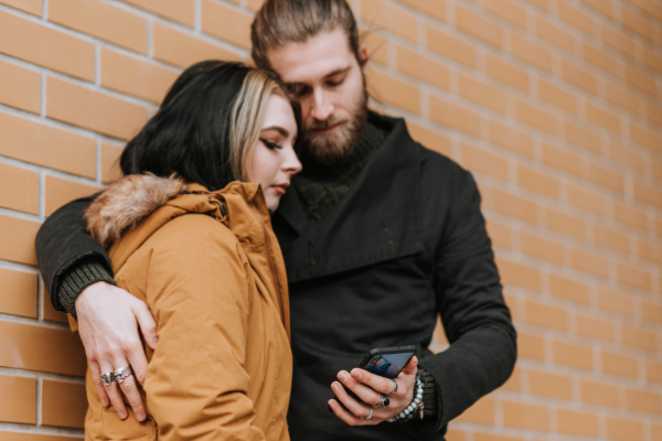 Casal abraçado com roupas de frio, olhando um celular