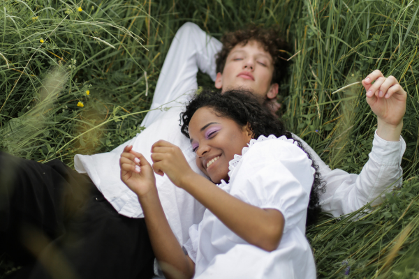 Menina deitada no peito de um menino. Os dois estão deitados na grama