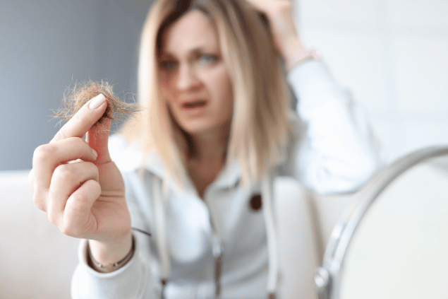 Mulher segurando fios de cabelo na mão. 