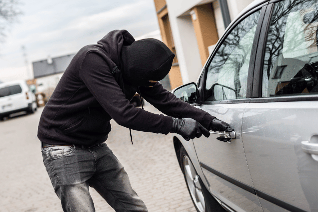Ladrão encapuzado tentando abrir a porta de um carro. 