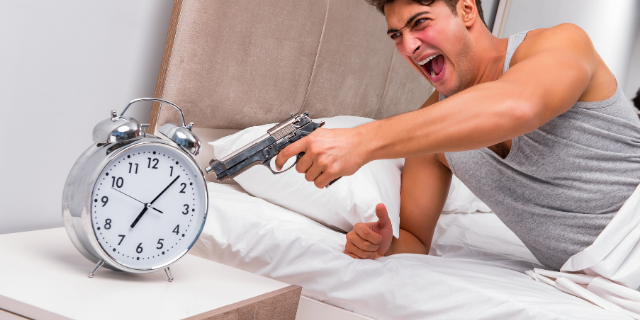 Homem deitado em uma cama aponta pistola para o despertador. 