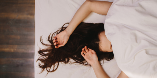Mulher deitada em cama com os braços acima do rosto e sobre o cabelo.