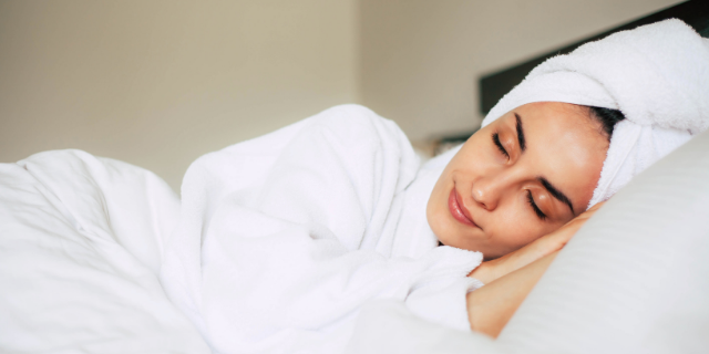 Mulher com uma toalha enrolada na cabeça dorme em cama.