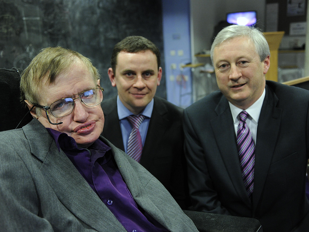 Stephen Hawking usando roupas sociais ao lado de dois homens