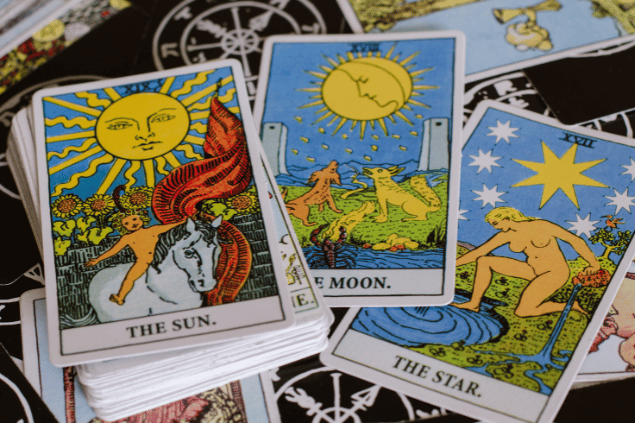 Há algumas cartas de Tarot sobre uma mesa: O Sol, A Lua e A Estrela. Embaixo delas, há um baralho com outras cartas.