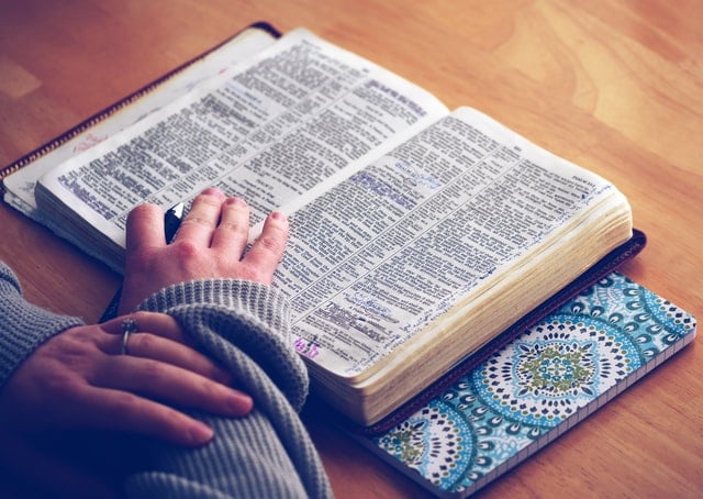 Bíblia aberta com mão branca feminina em cima.