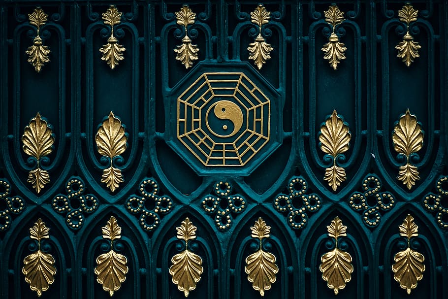 Arte em parede com desenhos dourados sobre uma superfície azul escura, com um símbolo do Yin e Yang no centro.