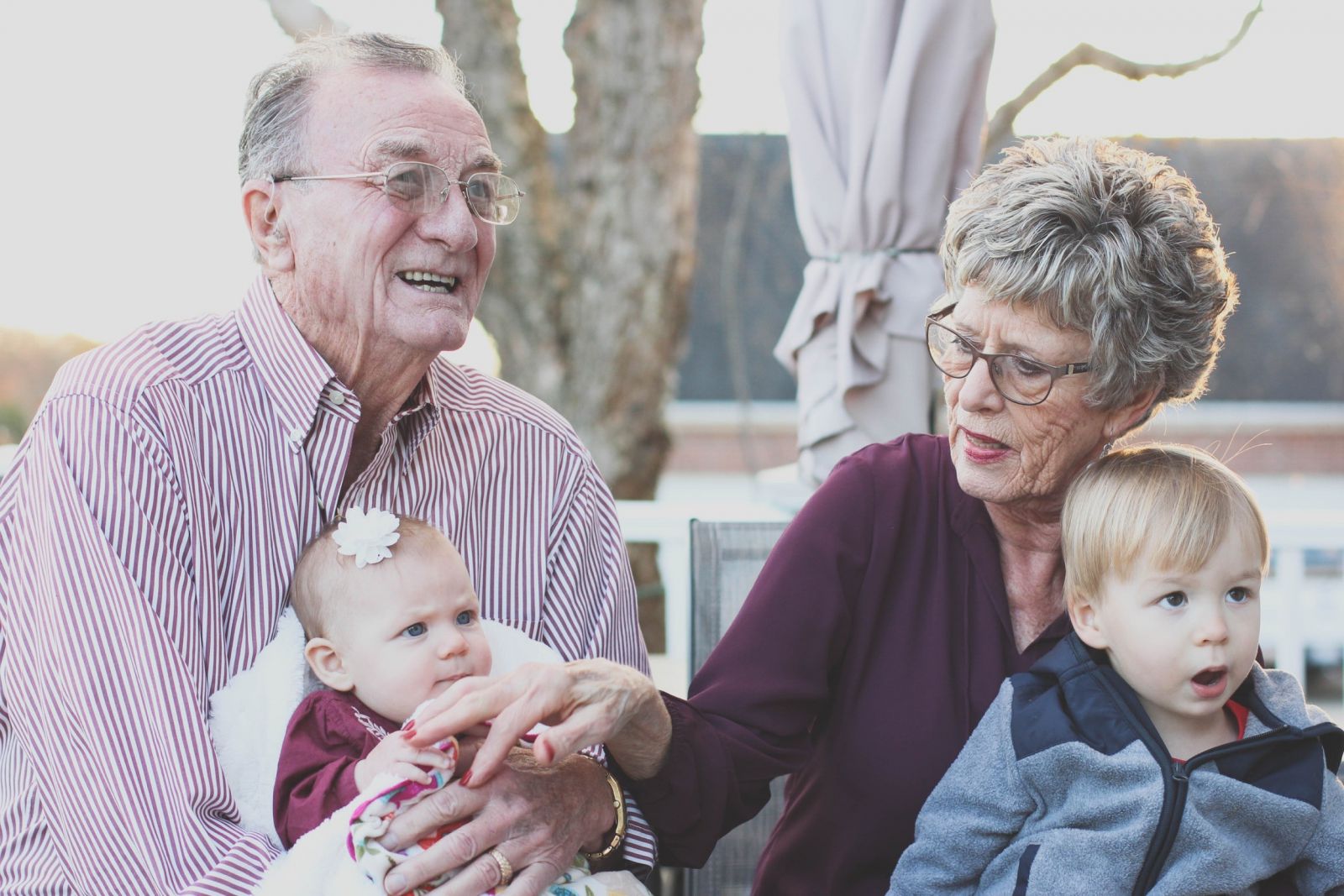 Avós sentados, sorrindo, com seus dois netos bebês em seus colos.