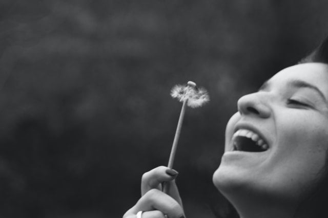 Mulher segurando flor dente-de-leão sorrindo em foto preto e branco