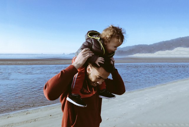 Pai segurando seu filho bebê nos ombros, na praia