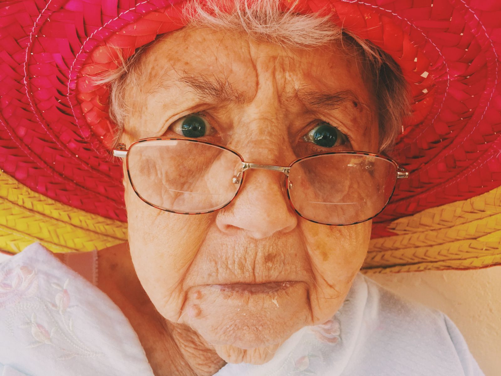Rosto de idosa branca de óculos e chapéu.
