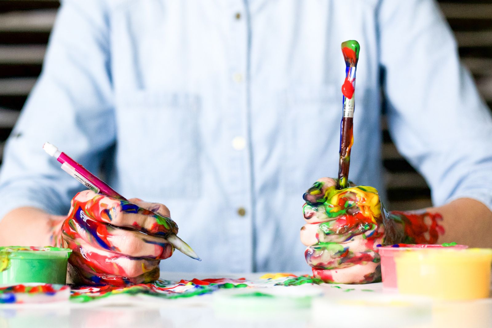 Pessoa segurando pincéis com tintas coloridas em suas mãos