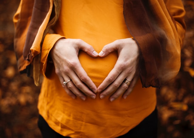 Mãos brancas femininas formando coração numa barriga grávida.