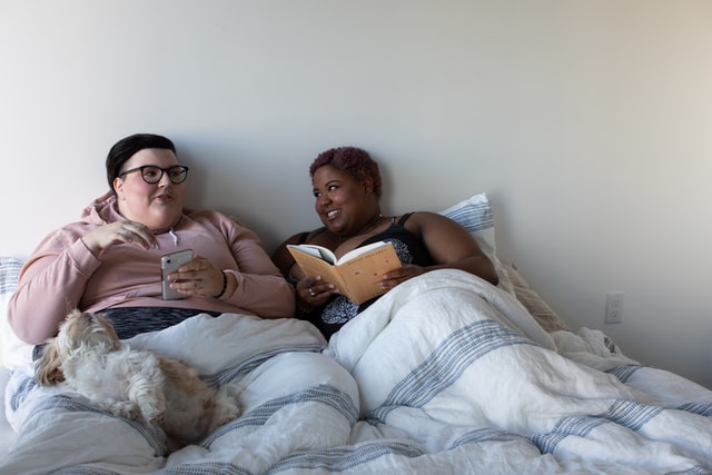 Mulher branca e mulher negra deitadas numa cama.