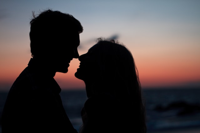 Silhueta de um homem e uma mulher se beijando ao pôr do sol.