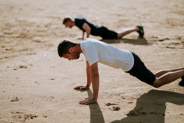 Homens fazendo flexões na praia.