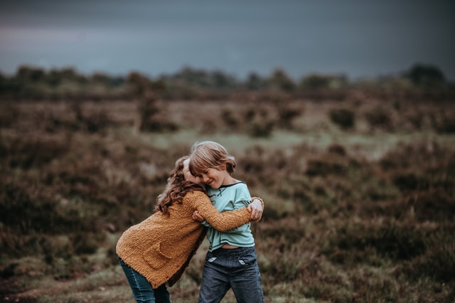 Menina e menino brancos abraçados num campo.