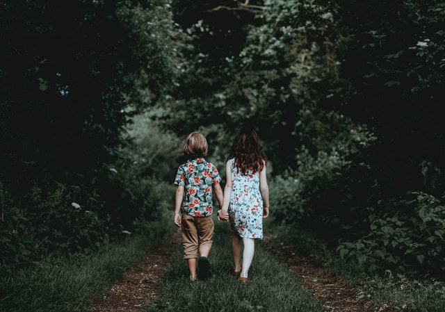 Menino e menina brancos de mãos dadas andando num bosque.