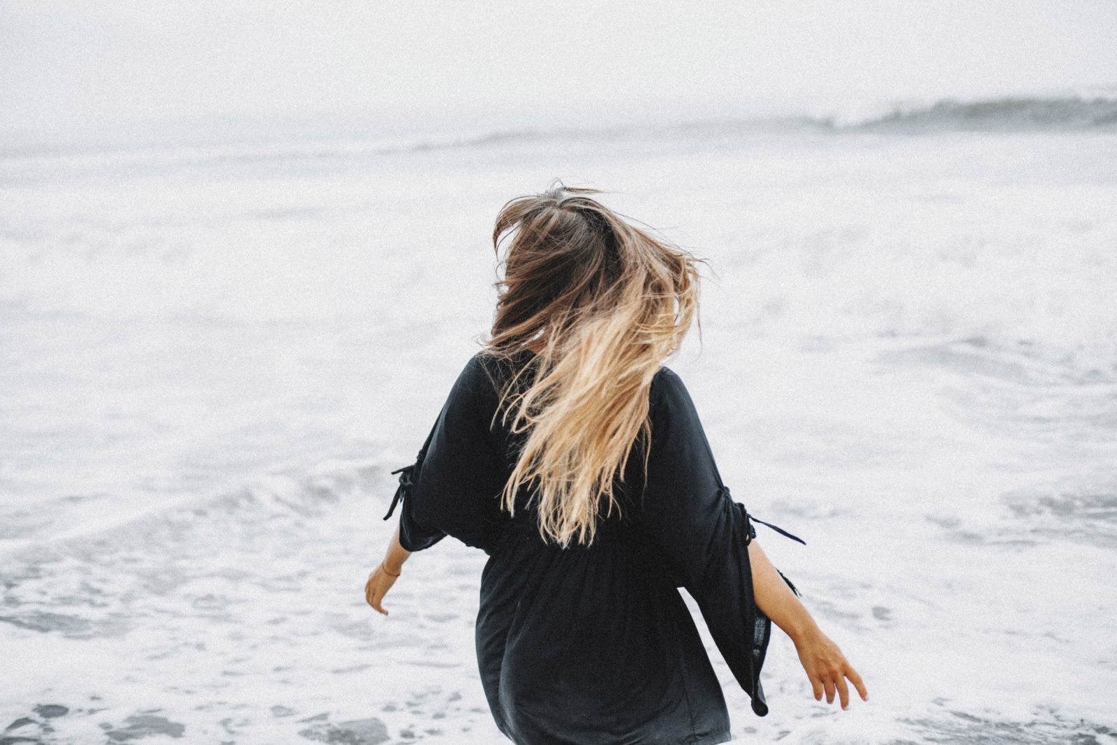 Mulher com os cabelos ao vento em frente ao mar.