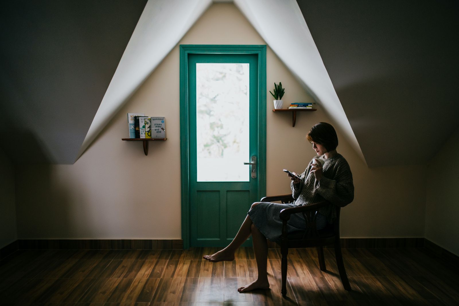 Mulher sentada em sua cadeira segurando um copo e celular ao lado da porta