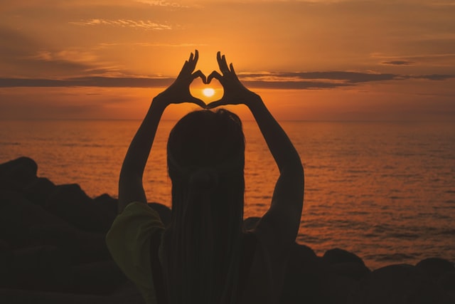 Silhueta de mulher formando coração ao redor do sol.