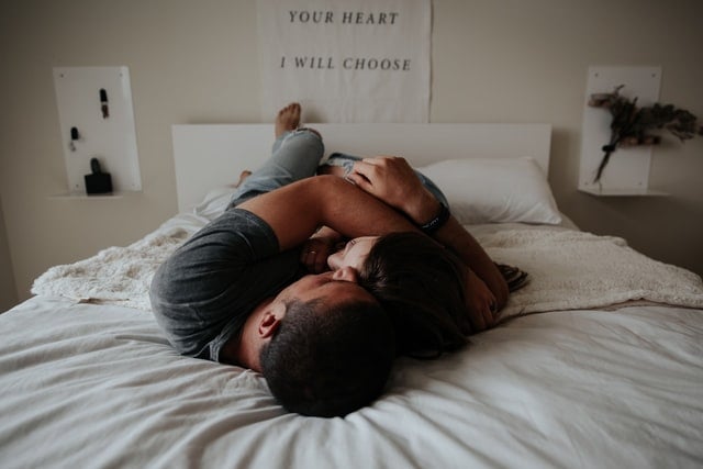 Homem e mulher brancos deitados numa cama abraçados.