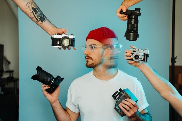 Homem branco segurando câmeras fotográficas.