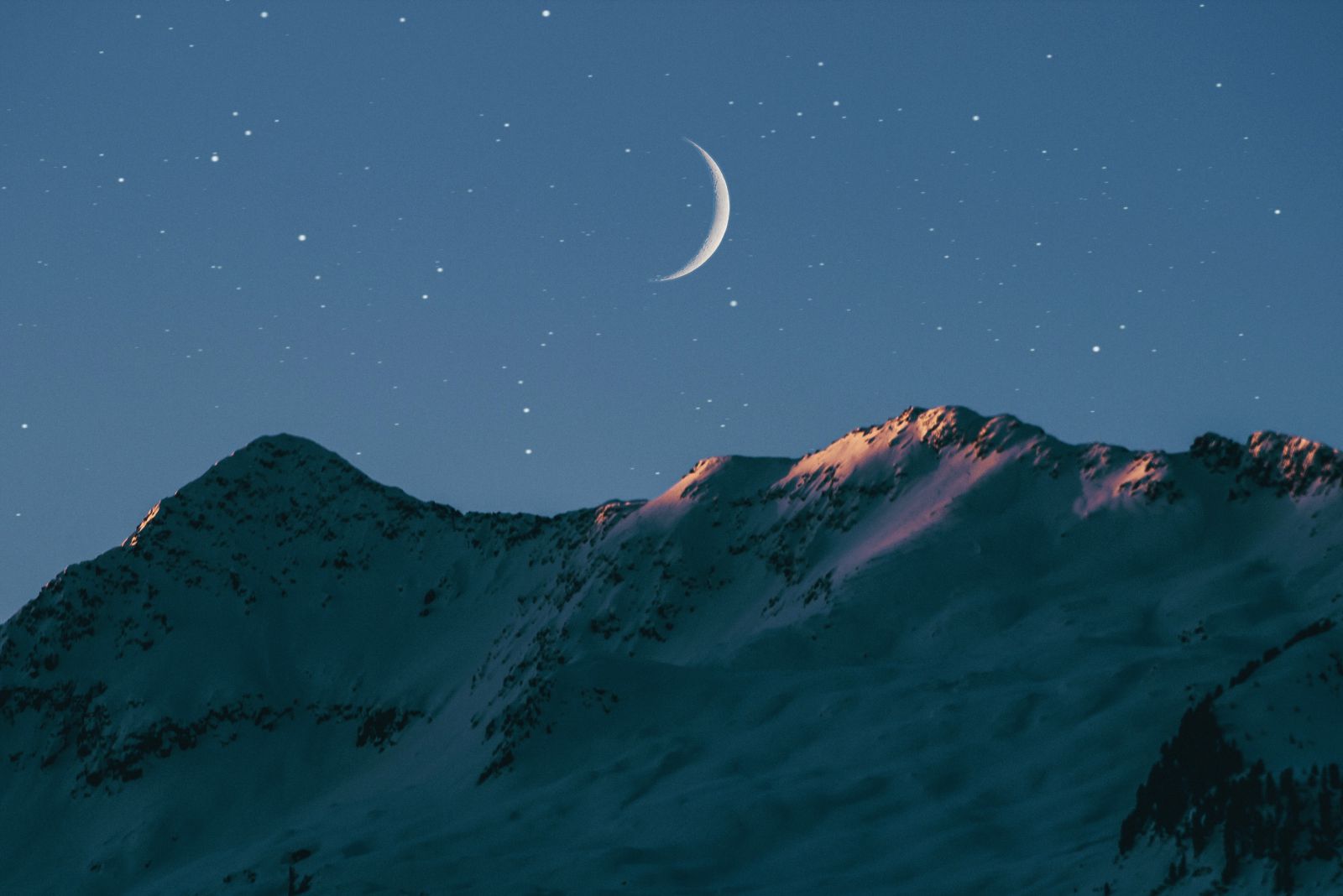 Lua minguante vista à noite, sobre paisagem montanhosa.