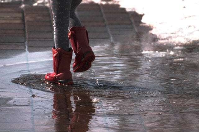 Pessoa com galochas pisando em água de chuva