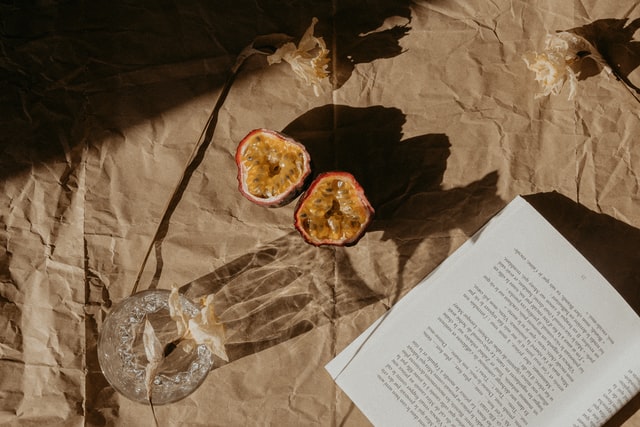 Maracujá cortado ao meio com copo e livro aberto ao sol